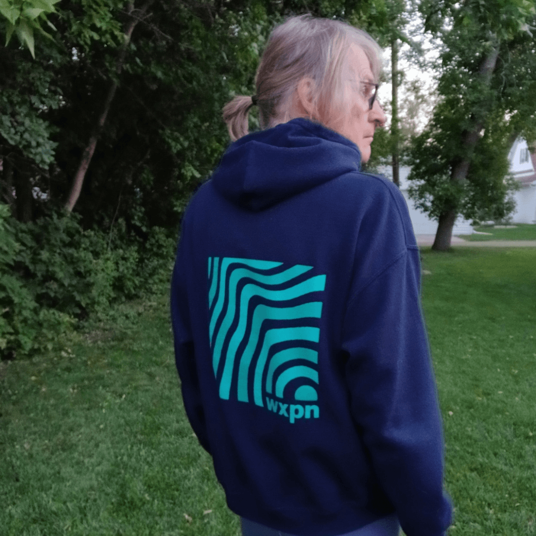 donor Mike Olson stands with his back in the middle of a grassy area with a blue WXPN hoodie